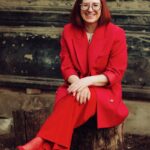 woman in red blazer and black skirt sitting on brown concrete stairs
